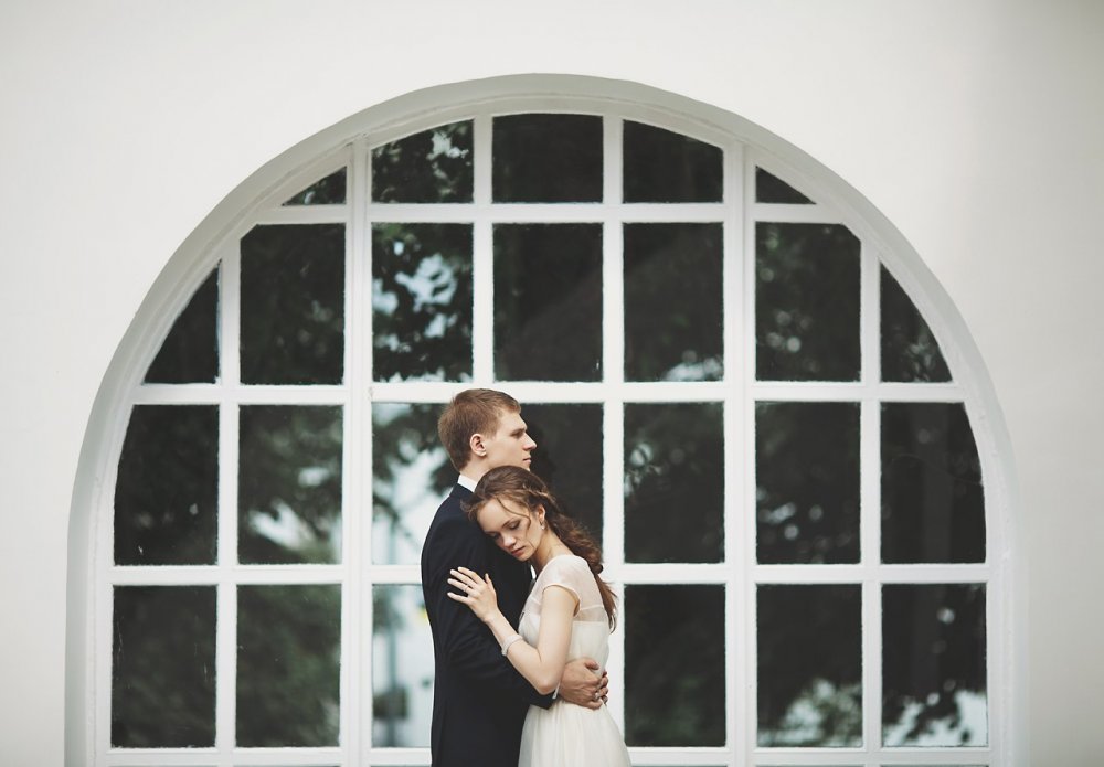 Фотосессия: невеста на плече у жениха на фоне решетчатых окон
